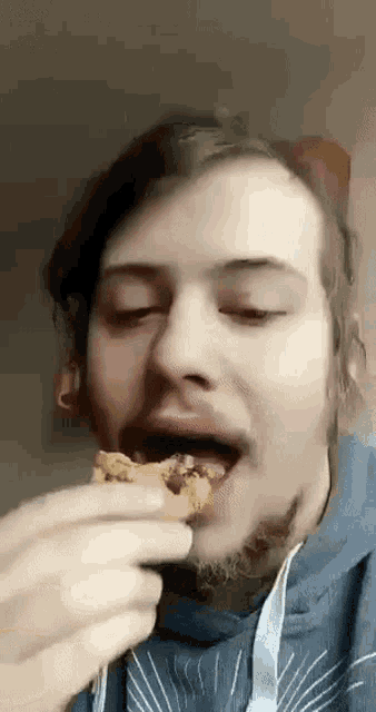 a man with a beard is eating a cookie with his eyes closed
