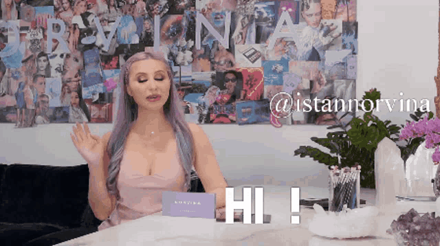 a woman with purple hair is sitting at a table with a sign that says hi on it