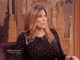 wendy williams is wearing a black polka dot dress and sitting in a purple chair .