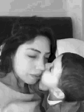 a black and white photo of a woman and a child kissing each other .