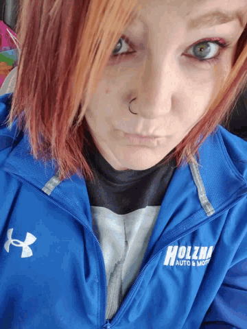 a woman wearing a blue under armour jacket that says ' holzman auto & moto ' on it