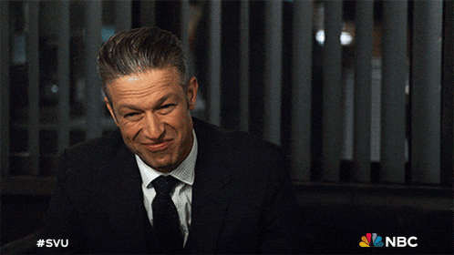 a man in a suit and tie is sitting in front of a nbc sign