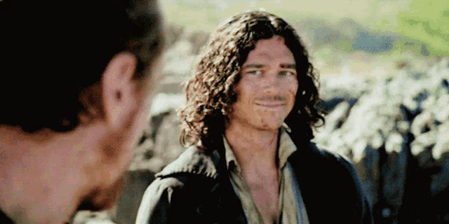 a man with long curly hair is smiling and talking to another man
