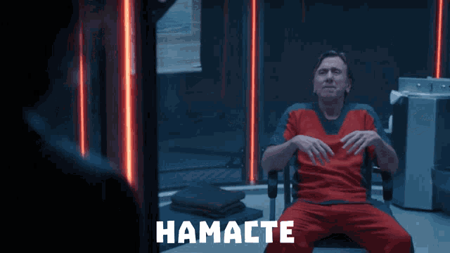 a man in a red scrub is sitting in a chair with the word hamacte on the bottom right