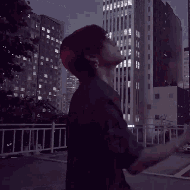 a man with red hair is standing in front of a city at night
