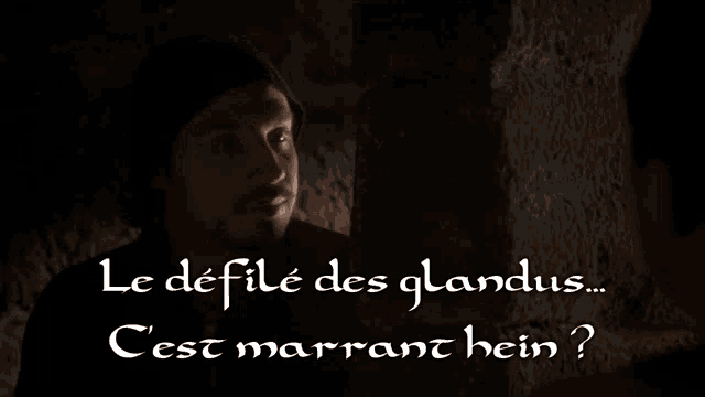 a man in a black hat is talking to another man in a dark room with the words le defile des glandus