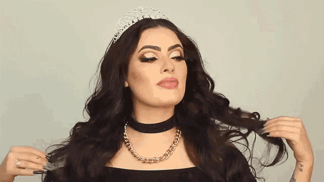 a woman wearing a tiara and a choker is touching her hair .
