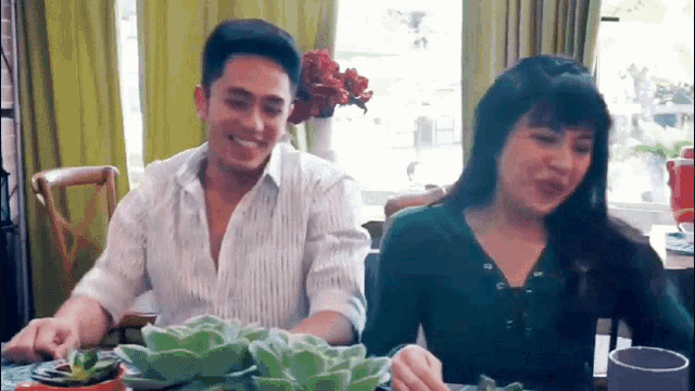 a man and a woman are sitting at a table with potted plants on it .