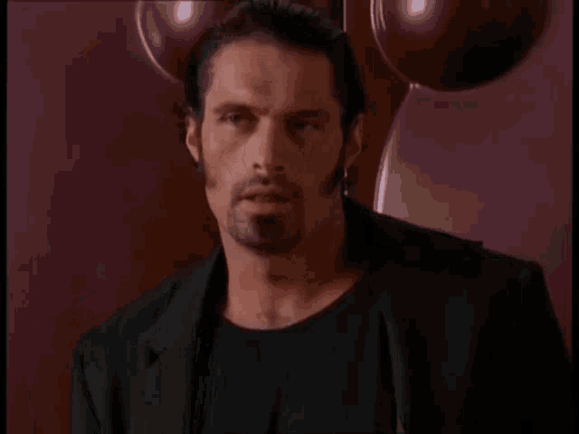 a man with a beard wearing a black shirt and a black jacket is pointing up