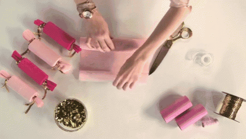 a woman is wrapping pink candy canes with ribbon and tape .