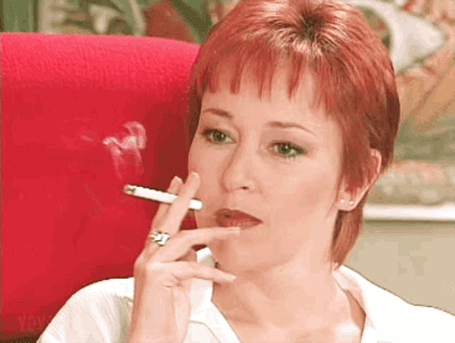 a woman with red hair is smoking a cigarette in a red chair