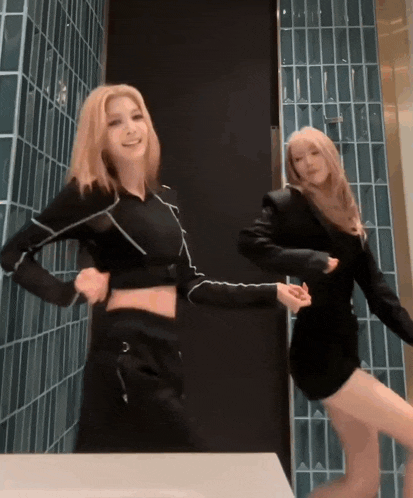two women in black clothes are dancing in front of a blue tiled wall