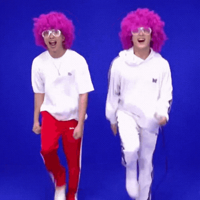 two men wearing pink wigs and glasses are dancing in front of a blue screen .