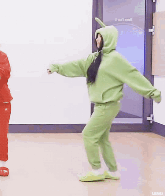 a woman in a green hoodie and green sweatpants is dancing in a room