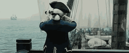 a man in a pirate uniform is looking through binoculars at a ship in the ocean .