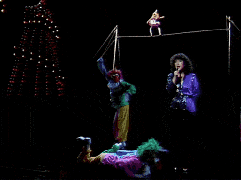a group of clowns are performing on a stage with a woman singing in front of them
