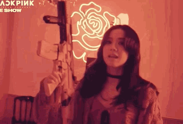 a woman is holding a gun in a room with a neon rose on the wall .
