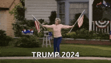 a woman is holding two american flags in front of a house and says trump 2024 .