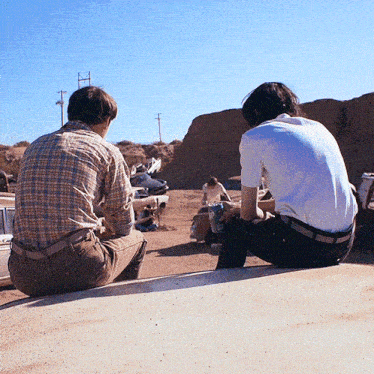 two men sit on the roof of a car looking at a pile of junk