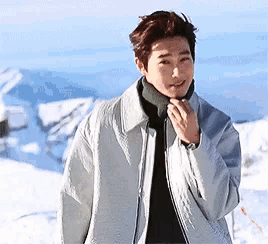 a young man wearing a white jacket and a black turtleneck is standing in the snow .