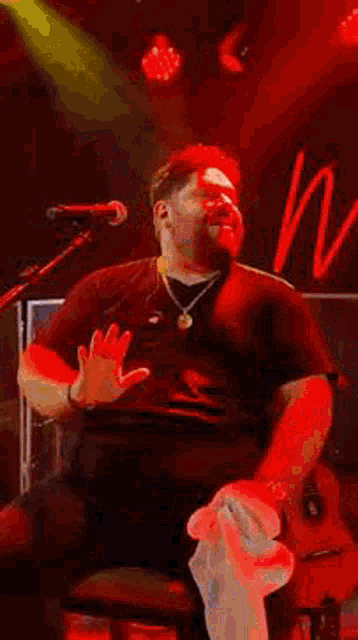 a man is sitting on a stool on a stage with a guitar and a microphone .