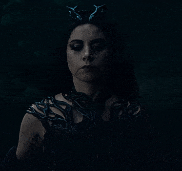 a woman with a crown on her head looks at the camera in the dark