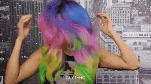 a woman with rainbow hair is wearing a green shirt with a guy tang logo on it .