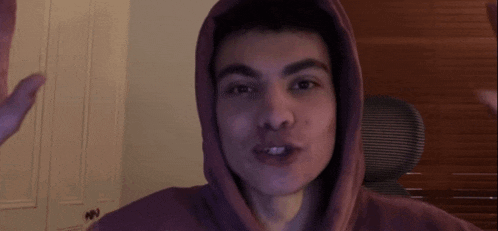a young man in a purple hoodie is waving his hands in front of a camera .