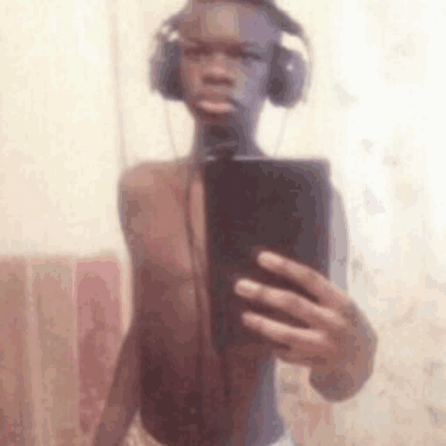 a shirtless man wearing headphones is taking a selfie with his cell phone