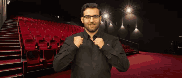 a man in a black shirt says " you 're welcome " in front of an auditorium full of red seats