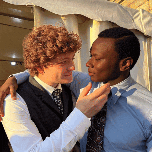 a man with curly hair and a man with black hair are hugging each other