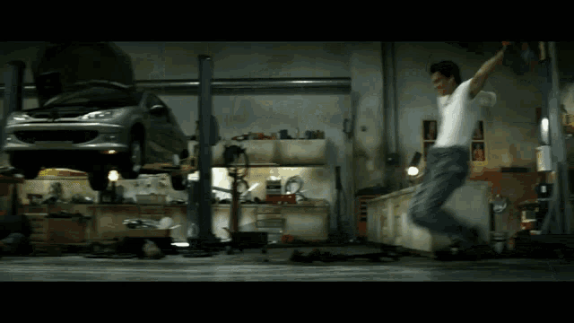 a man is jumping in the air in a garage with a car on a lift