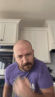 a bald man with a beard wears a purple shirt with the letter a on it