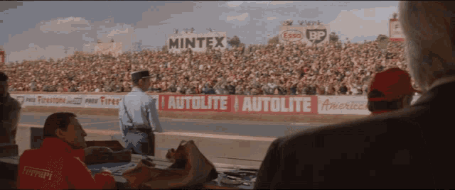 a man in a ferrari jacket watches a race from the sidelines