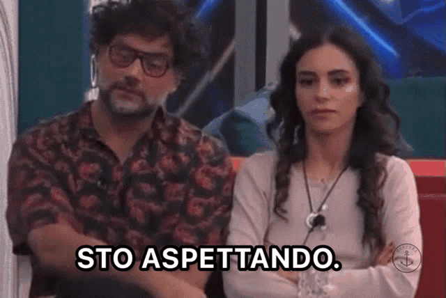 a man and a woman are sitting on a couch with their arms crossed and a caption that says sto aspettando