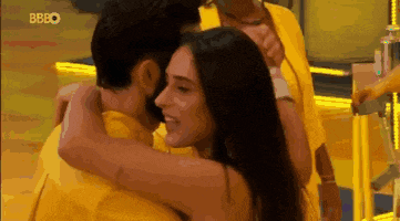 a man and a woman are hugging each other in a room . the man is wearing a yellow shirt .