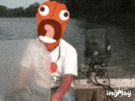 a man wearing an orange face mask is standing next to a boat motor