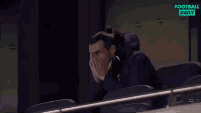 a man is sitting in a stadium covering his face with his hands while watching a football game .