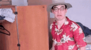 a man wearing a hat and a hawaiian shirt is standing in front of a closet .