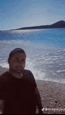a man in a black shirt is standing on a beach near the water