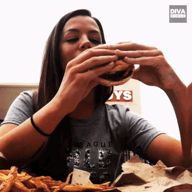 a woman eating a hamburger in front of a sign that says boys