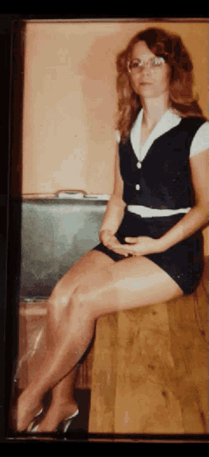 a woman sitting on a table with her legs crossed and a suitcase in the background