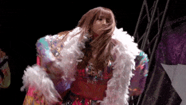 a woman is wearing a feathered coat and dancing on a stage