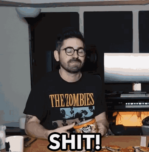 a man wearing a shirt that says the zombies is sitting at a table