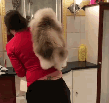 a woman in a red shirt is holding a cat on her back in a bathroom