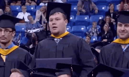 a man in a graduation cap and gown is holding a laptop in front of a crowd of people .