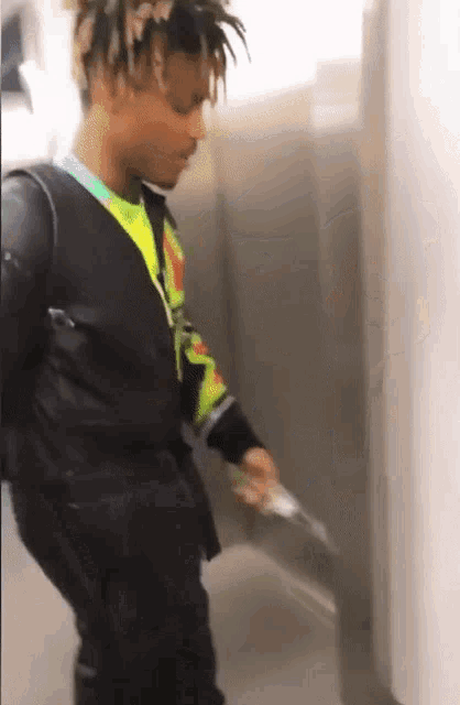 a man with dreadlocks is standing in a hallway holding a gun .