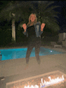 a woman is standing in front of a fire pit next to a pool .