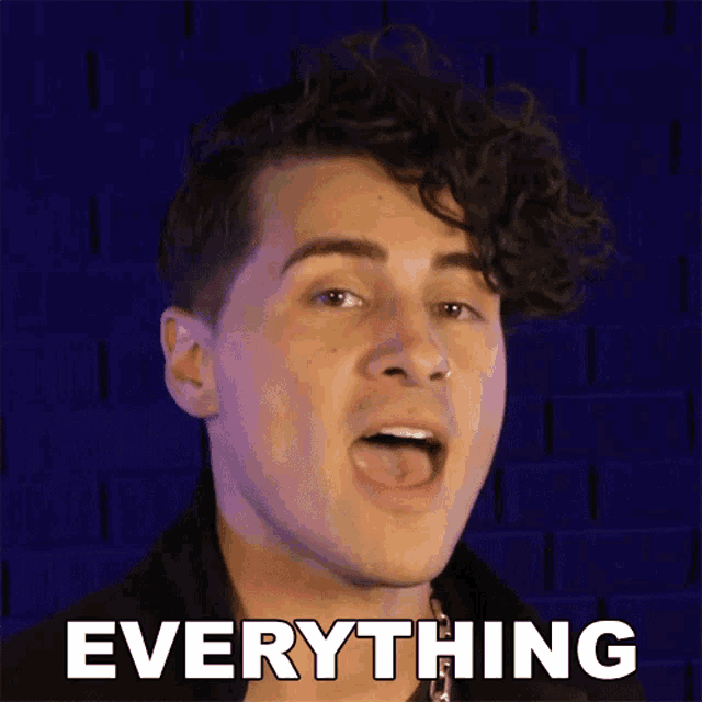 a man with curly hair says everything in front of a blue wall