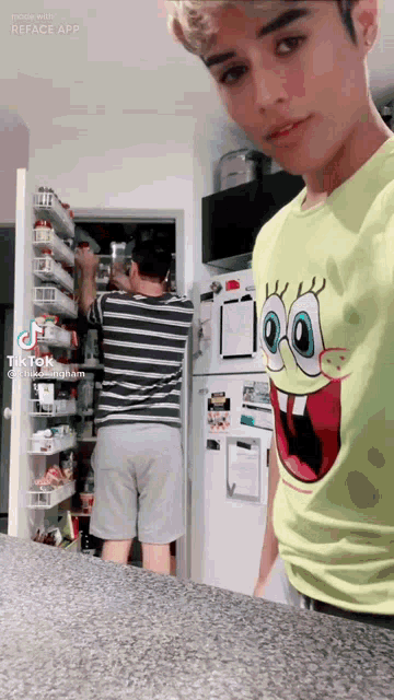 a man in a spongebob shirt is standing next to another man in a striped shirt in a kitchen .